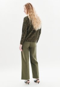 Maglione leopardato in verde oliva, abbinato a pantaloni larghi a vita alta sempre in verde oliva e mule con tacco neri, realizzati con tessuti testurizzati.