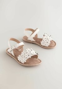 Sandali bianchi con decorazioni floreali sulle cinghie, cinturino alla caviglia regolabile e soletta in finta suede marrone. Design con suola piatta.