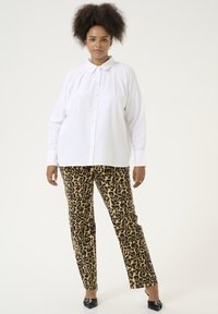 Chemise blanche à boutons avec col, coupe ample ; associée à un pantalon léopard beige ; modèle portant des chaussures à talons noires.