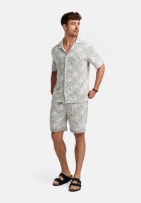 Leichte Kurzarm-Hemd mit Knopfleiste und passende Shorts in einem grauen, strukturierten Muster; kombiniert mit dunklen Sandalen.