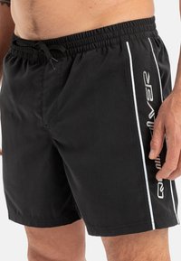 Bañador negro con cinturilla elástica y cordón. Presenta rayas blancas en los laterales y un logotipo impreso en el lado derecho.