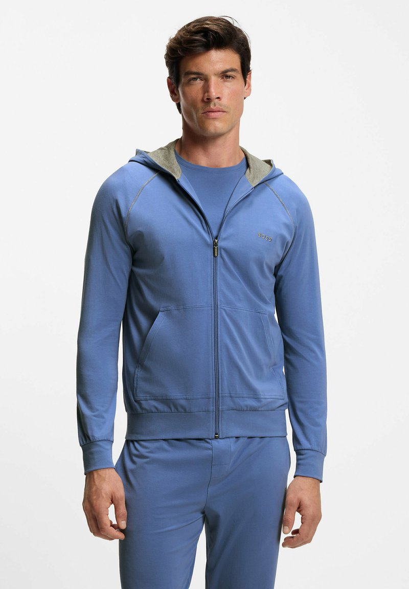 Light blue zip-up hoodie with a gray lined hood, front pockets, and ribbed cuffs. Worn over a matching blue shirt. Smooth fabric texture.