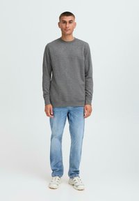 Maglione grigio con collo rotondo e maniche lunghe, abbinato a jeans azzurri chiari e sneakers bianche. Design semplice con una texture liscia.