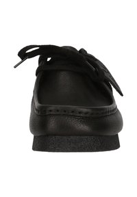 Mustat nahkakengät, joissa on pyöristetty varvas, litteä, teksturoidut pohjat ja mustat nauhat. Vähäistä ompelua reunassa.