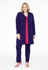 Mørkeblå lang cardigan med seks knapper, lagd over en lys pink top og matchende mørkeblå bukser, suppleret med pink højhælede sandaler.