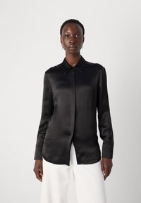 Camicia nera in satin con maniche lunghe, colletto a punta e bottoni davanti. Tessuto liscio, finitura leggermente lucida e vestibilità comoda.