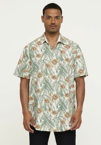 Korte mouwen shirt met een bloemen- en bladpatroon in groen en geel op een witte achtergrond, gemaakt van lichte stof.