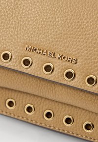 Sac à main en cuir beige avec quincaillerie dorée et accents de rivets. Présente le nom de marque "MICHAEL KORS" en relief à l'avant.