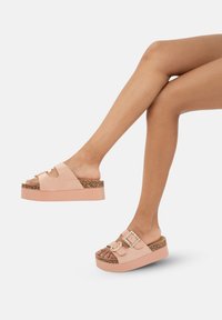 Sandali platform in un delicato rosa pallido con dettagli in sughero, accenti a doppia fibbia e punte aperte, caratterizzati da una superficie liscia e una suola testurizzata.