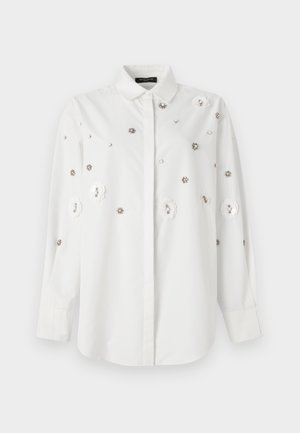 Chemise blanche à manches longues avec col, ornée d'appliqués floraux et de sequins décoratifs. Tissu lisse avec une coupe ajustée.