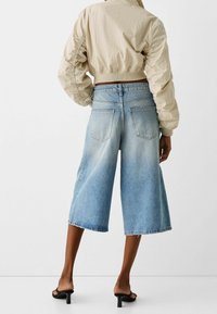 Beige cropped bomber jacket with ruched sleeves paired with wide-leg denim culottes in light blue, featuring frayed hem and back pockets.
