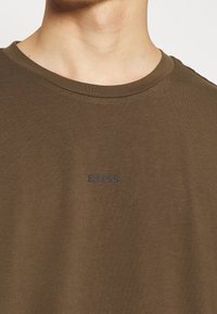 Olivgrön bomullströja med rund halsringning och korta ärmar. Har en diskret "BOSS"-logotyp i mörk marinblått på framsidan.