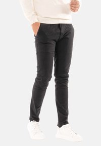 Pantaloni neri slim-fit realizzati in tessuto misto cotone, con una texture liscia e un classico design a cinque tasche. Indossati con sneakers bianche.
