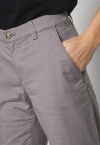 Ljusgrå byxor i ett mjukt tyg. Har knappstängning och sidofickor. Midjebandet har hällor för bälte och diskreta sömdetaljer.