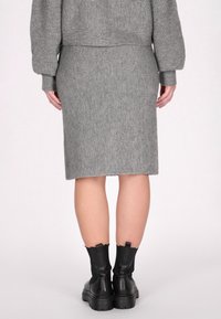 Grauer Strickrock mit gerippter Textur, knielang, kombiniert mit schwarzen, klobigen Stiefeln mit Absatz. Sichtbare Nahtdetails und taillierter Schnitt.