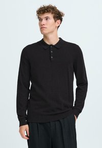 Črna dolge rokave polo majica, pleten material, običajen kroj, tri gumbe na zapenjanju, rebrasti manšeti in rob, gladka tekstura.