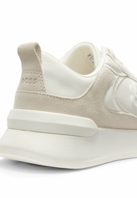 Beige sneaker med en kombination af glatte og teksturerede materialer, en kraftig hvid sål og en diskret logodetalje på hælen.