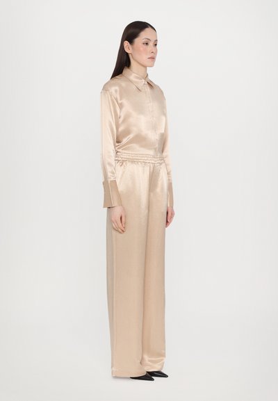 Beige satin outfit featuring a collared, button-down shirt and elastic waist, wide-leg pants. Includes pointed black shoes. Smooth texture.