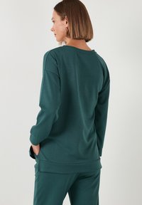 Zöldeskék, hosszú ujjú pulóver, laza szabással, kerek nyakkivágással és oldalsó hasítékokkal, puha, textúrált anyagból készült, eső vállakkal.
