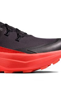 Scarpa sportiva nera e rossa con tomaia testurizzata, intersuola spessa rossa e suola in gomma con motivo. Presenta occhielli per i lacci in contrasto.