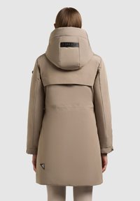 Bežna podložena parkas z veliko kapuco, zadnjim ventilom in blagovno znamko. Tkanina ima gladko teksturo z elegantnim, sodobnim dizajnom.