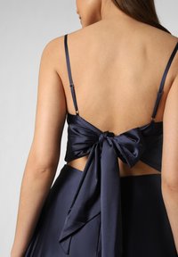 Navy Satin-Top mit dünnen Trägern, gekennzeichnet durch eine große Schleifenapplikation am Rücken, offenes Rücken-Design und glatte Textur.