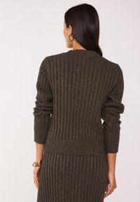 Pull en maille côtelée marron avec un col rond, des manches longues et de subtiles paillettes métalliques. La texture est douce, avec une silhouette ajustée.