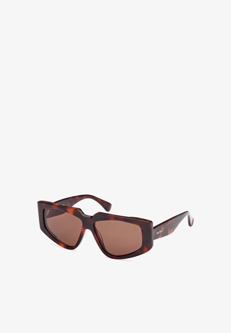 Bruna sköldpaddsglasögon med en geometrisk ram, mörkbruna linser och smala skalmar med en logotyp på sidan.