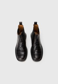 Botas de tobillo de cuero negro con patrón de cocodrilo, paneles laterales elásticos y forro interior color marrón claro, vistas desde arriba sobre un fondo blanco.