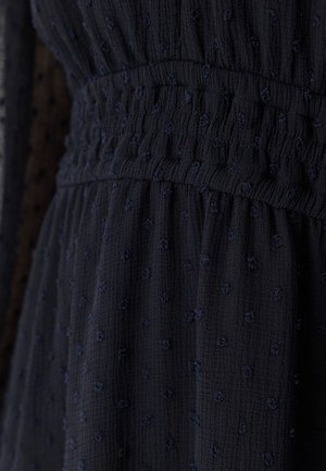 Navyfarbendes, texturiertes Kleid mit gesmoktem Taillenbereich und kleinen gestickten Punkten. Verfügt über einen weichen, kräuseltartigen Stoff und eine fließende Silhouette.