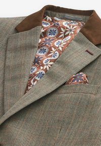 Brun houndstooth blazer med en brun ruskinds krave. Foret med et blomsterprintet stof i blå og orange nuancer. Inkluderer en matchende lommefyr.