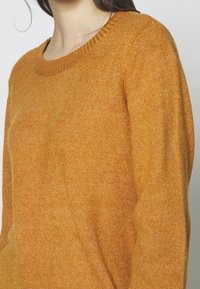 Maglione arancione a maglia con scollo rotondo, colletto a coste e maniche lunghe, caratterizzato da una texture morbida e un colore uniforme in tutto.