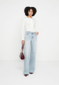 Camisa branca de mangas compridas com botões, jeans azul claro de cintura alta e pernas largas, e uma pequena mala bordô. Sapatos de salto completam o conjunto.