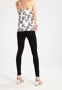 Jean noir skinny associé à un débardeur blanc avec un motif de feuilles noires et des bretelles fines. Chaussures à talons carrés argentés.