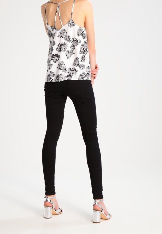 Jean noir skinny associé à un débardeur blanc avec un motif de feuilles noires et des bretelles fines. Chaussures à talons carrés argentés.