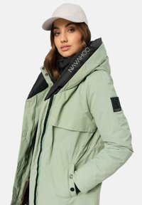 Light green parka jacket with a black interior, featuring a large hood, front snap pockets, and zip closure, accented with contrasting stitching.