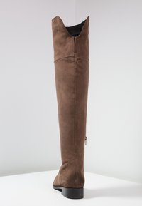 Brązowy zamszowy kozaki za kolano o prostej sylwetce, z wyraźnymi przeszyciami i suwakiem z tyłu przy pięcie.