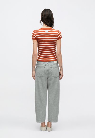 Κόκκινο και λευκό ριγέ κοντομάνικο πουκάμισο, εφαρμοστή σχεδίαση, σε συνδυασμό με ανοιχτό γκρι, άνετο τζιν και μπεζ παπούτσια τύπου slip-on.