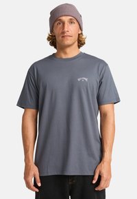Grå bomulds t-shirt med rund hals og korte ærmer, prydet med et lille hvidt logo print på venstre bryst. Enkel, afslappet pasform design.