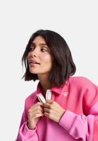 Rosa polo sweatshirt med gradientdesign, med hvit krage og hjerte-logo. Myk stoffkvalitet med avslappet passform. Lange ermer.