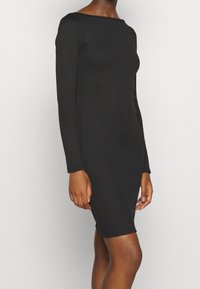 Robe noire à manches longues côtelées avec un col bateau, une coupe ajustée et une longueur genou. Texture lisse sans motifs ni accents visibles.