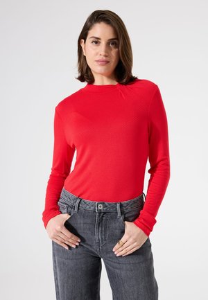 Haut rouge à manches longues en tissu texturé, col rond et coupe slim, associé à un jean en denim gris taille haute.