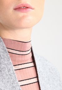Gray knit cardigan draped over a ribbed, pink turtleneck with thin black stripes. Smooth fabric textures and close-fitting design.