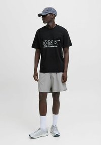 Sort t-shirt med hvid "CNZ" logo, lysegrå shorts, sølvfarvede træningssko og en grå mønstret kasket. Enkel, afslappet sportstøj.