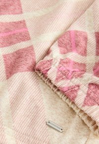 Rozā un krēma rakstainais audums ar rūtiņu dizainu un mīkstu faktūru. Iezīmēts ar metāla birku ar uzrakstu "DOWNTIME", kas ir iešūta.