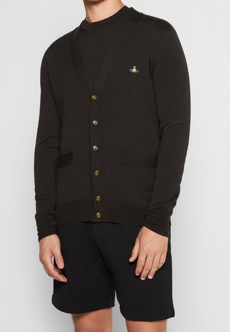 Svart stickad cardigan med v-ringning, fem bruna knappar, två framfickor och en liten broderad logotyp på vänster bröst.