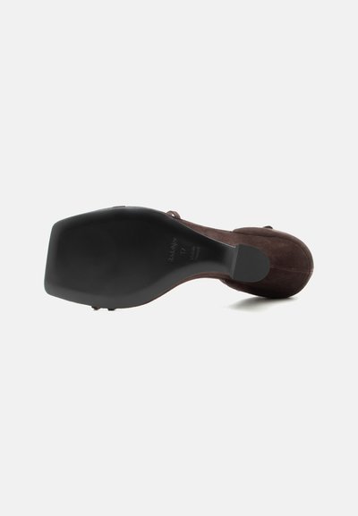 Chaussure à talon haut en suède marron vue depuis la semelle, montrant une partie inférieure noire lisse avec des indications de taille et de marque.