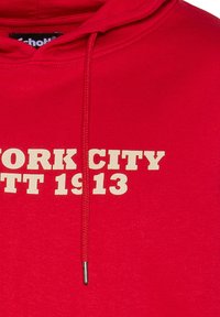 Sudadera roja de algodón con una tela texturizada. La parte frontal presenta un texto en color crema: "NUEVA YORK EST. 1913," y un detalle de cordón.