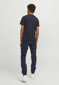 T-shirt en jersey marine à col rond associé à un pantalon cargo marine. Le pantalon est doté de poches et de poignets élastiques. Le modèle porte des baskets blanches. Simple et décontracté.