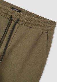 Oliwkowe dresy z elastycznym paskiem w talii, sznurkiem do regulacji, bocznymi kieszeniami oraz gładką fakturą. Metka informuje "Terranova".